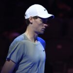 Jannik Sinner con uno sguardo concentrato e un cappello bianco
