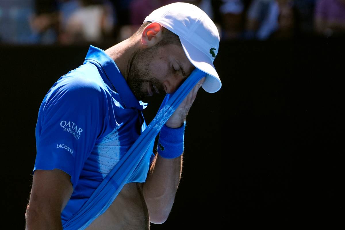<ovak Djokovic con cappellino e mentre di deterge la fronte dal sudore con un lembo della maglietta