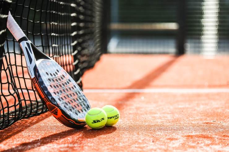 Racchetta da padel appoggiata alla rete e due palline