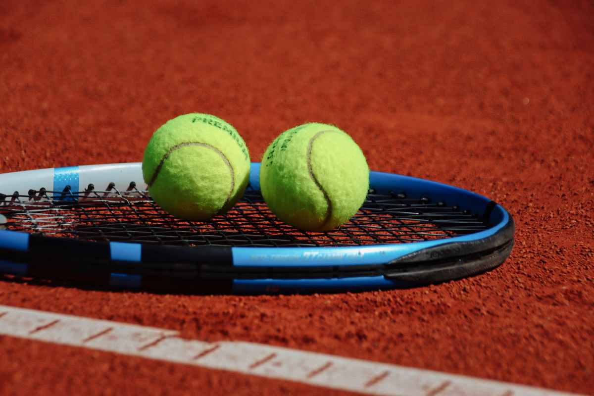 Racchetta e due palline da tennis appoggiate sulla terra rossa