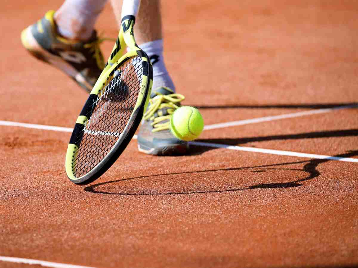 giocatore tennis raccoglie la pallina con la racchetta
