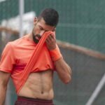 Novak Djokovic si porta la maglia sul viso durante un match