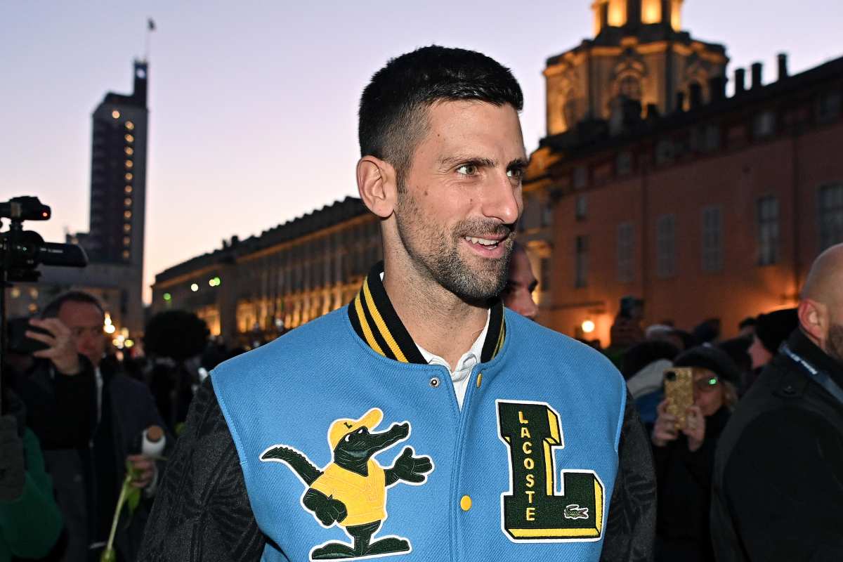 Novak Djokovic sorridente, che indossa una giacca azzurra, nera e gialla
