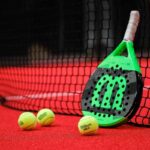 Racchetta da padel appoggiata alla rete e tre palline