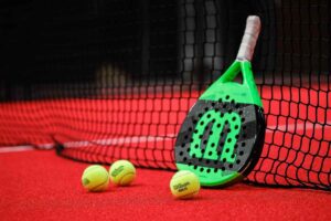 Racchetta da padel appoggiata alla rete e tre palline