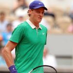 Jannik Sinner con una maglia verde e un cappello blu