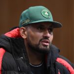 Nick Kyrgios in conferenza stampa con cappello verde e giubbotto nero e rosso