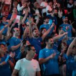 Tifosi italiani vestiti d'azzurro sbandierano il tricolore ed alzano le mani al cielo