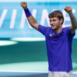 Cobolli, con la maglia azzurra, sorride ed alza le braccia al cielo dopo una vittoria