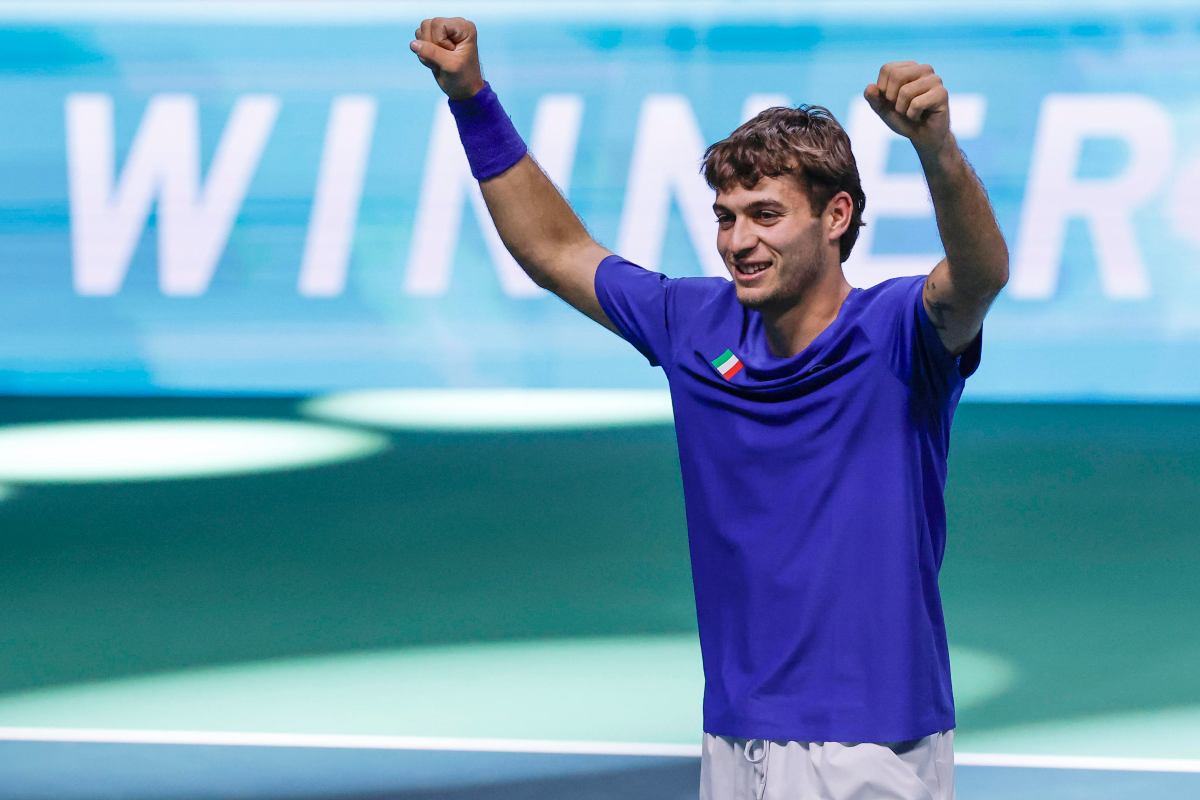 Cobolli, con la maglia azzurra, sorride ed alza le braccia al cielo dopo una vittoria